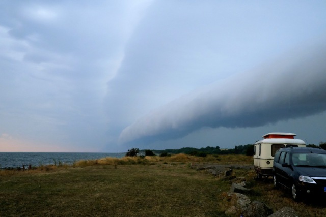 Picture of a car and a 1980s caravan close to the baltic sea shore.  There's an impressive thunderstorm rolling in.